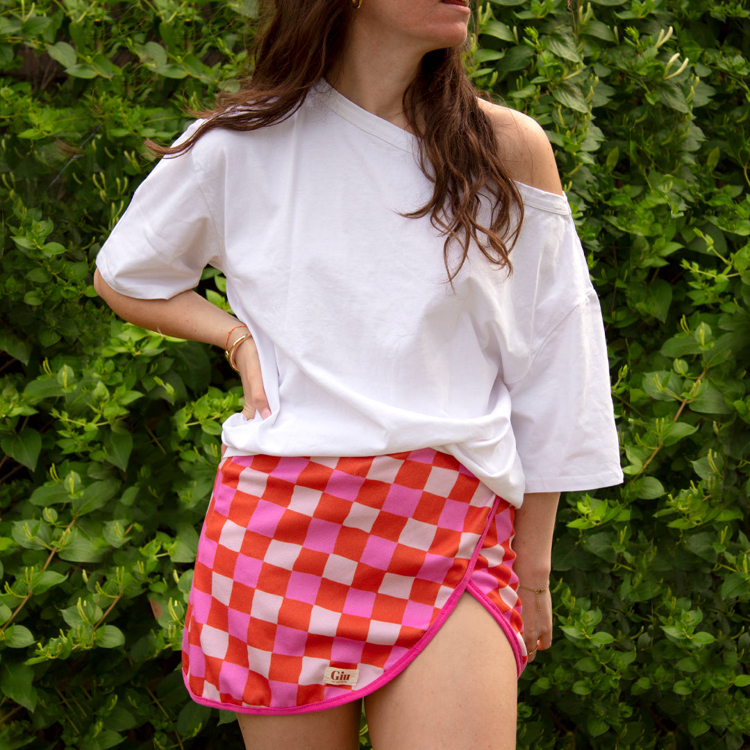 Jupe de plage éponge Giu portée, coupe portefeuille, liens noués dans le dos, damier orange fuchsia